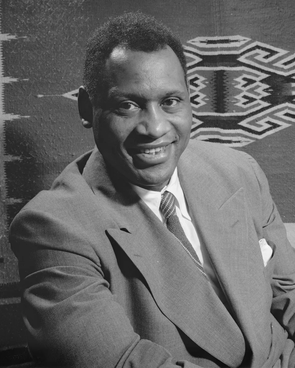 Paul Robeson smiling, seated in a suit and tie.